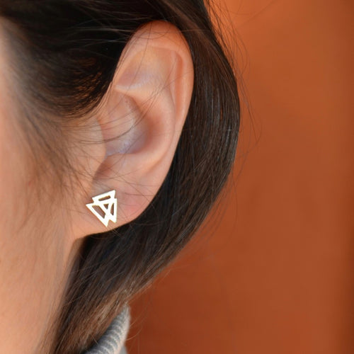 Close-up of an ear wearing a geometric silver earring against an orange background