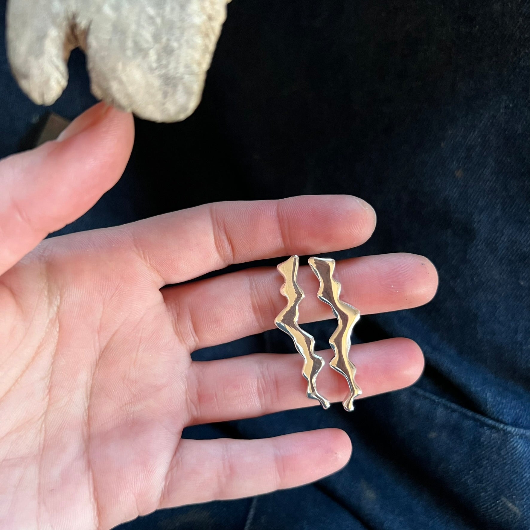Handmade silver earring held in the craftswoman’s hand