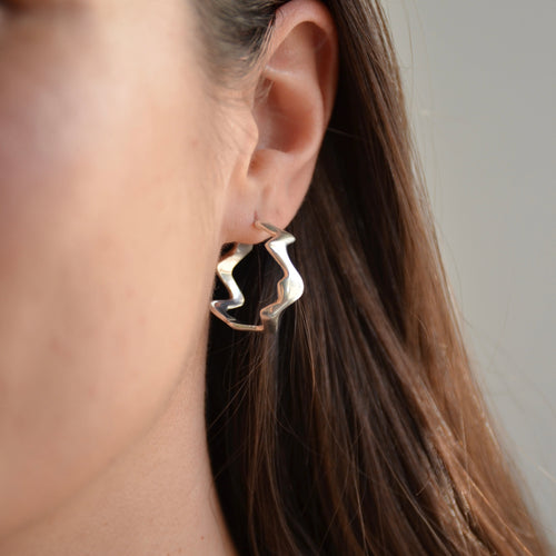 Close-up of a person wearing a pair of silver hoop earrings with a plain background