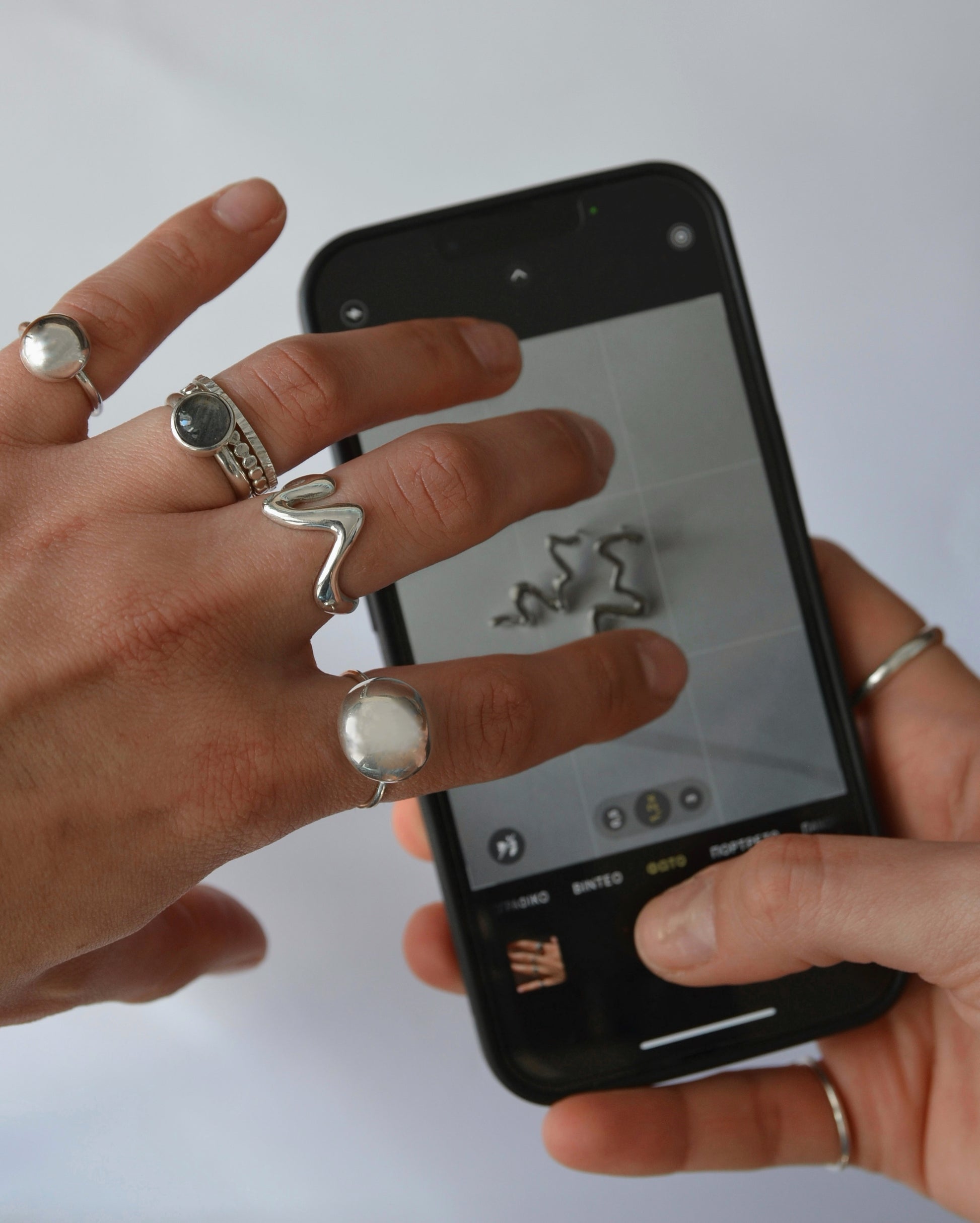 Person holding a smartphone with jewelry displayed on the screen, wearing multiple handmade silver rings.