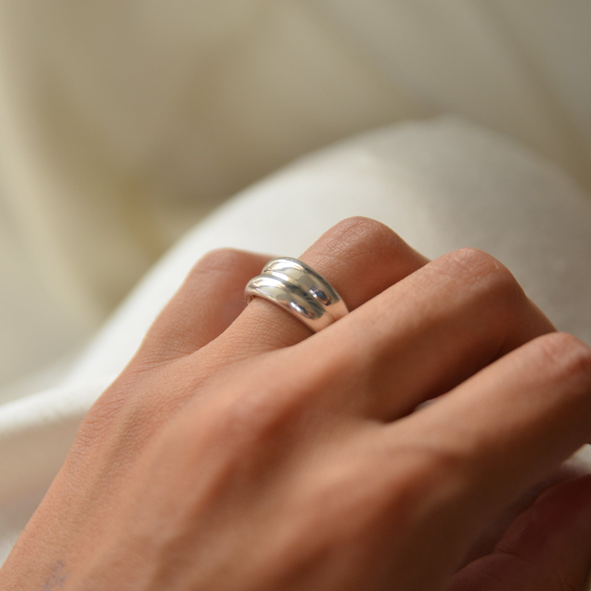 Handmade curvy silver ring on a woman's finger with a soft beige background