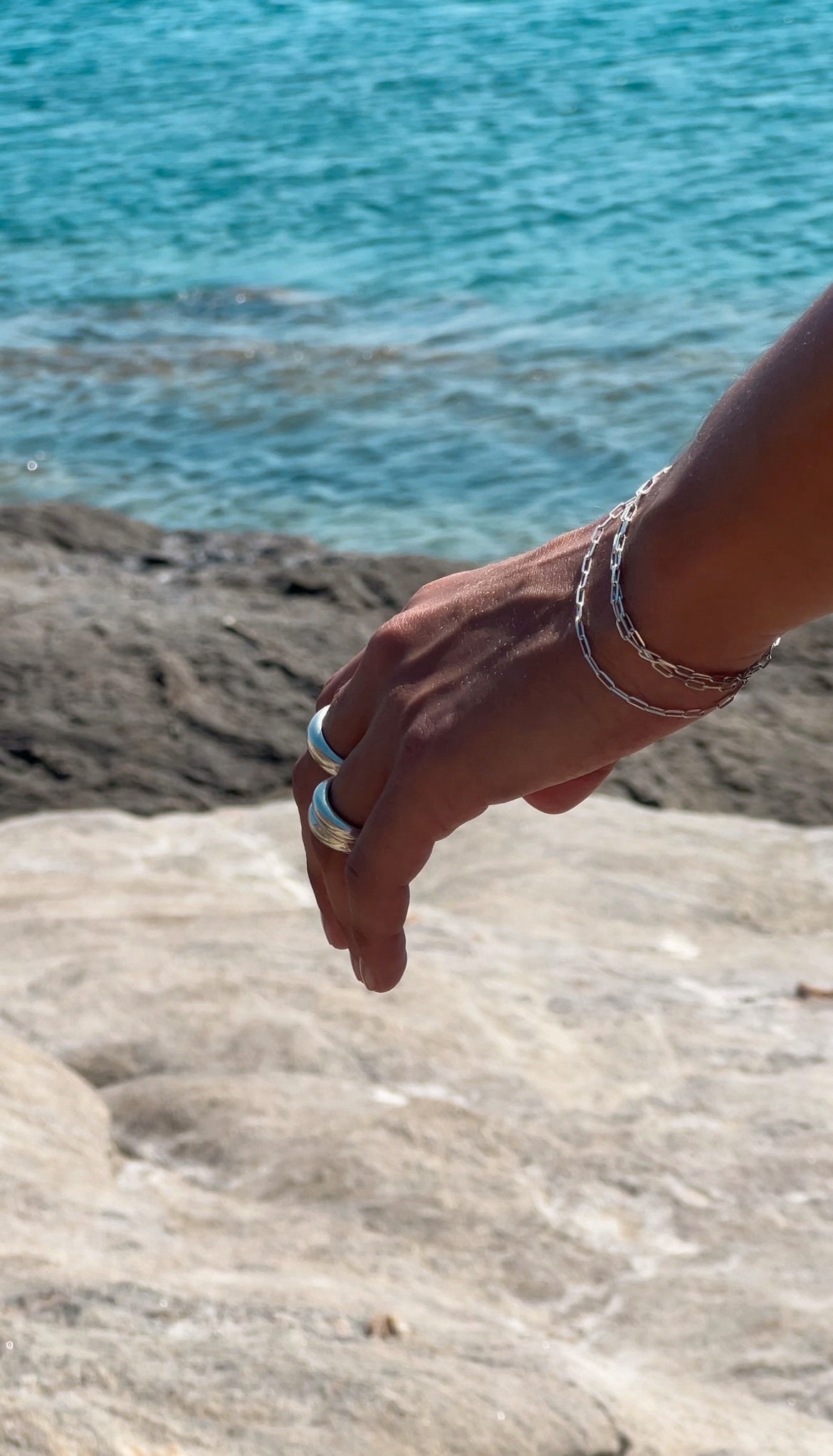 Hand with silver rings and bracelets by a body of water