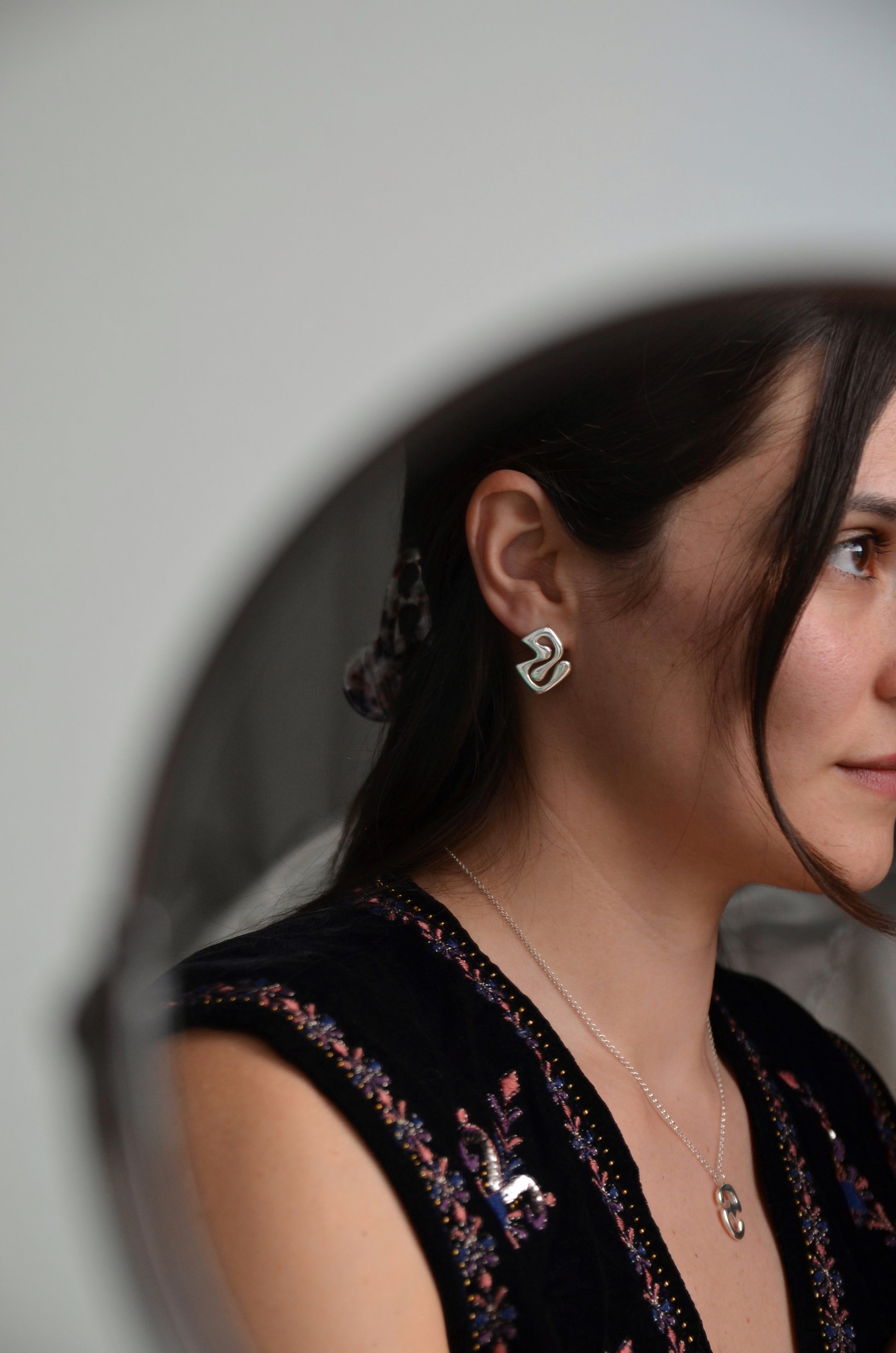 Woman wearing silver handmade earrings, looking into a mirror.